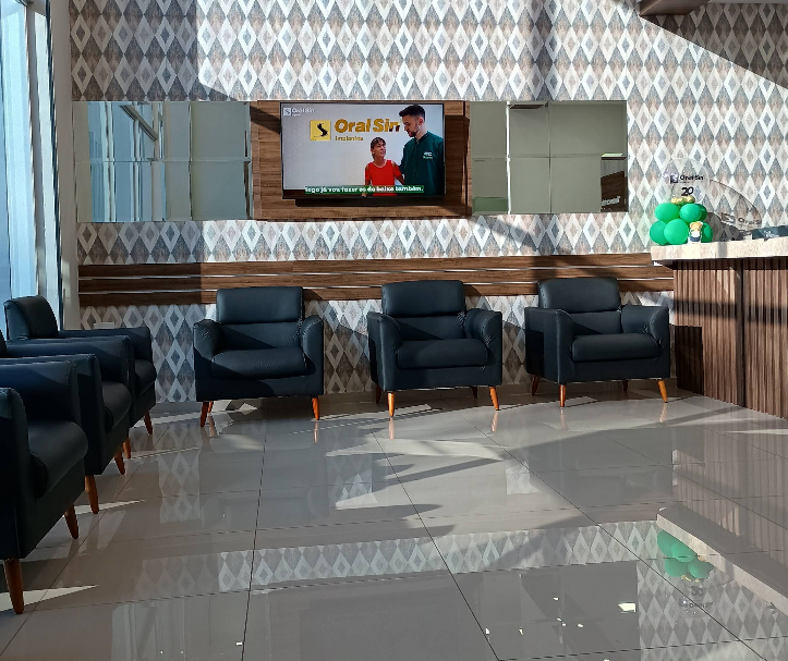Recepção e sala de espera com poltronas escuras, painéis de madeira e TV.